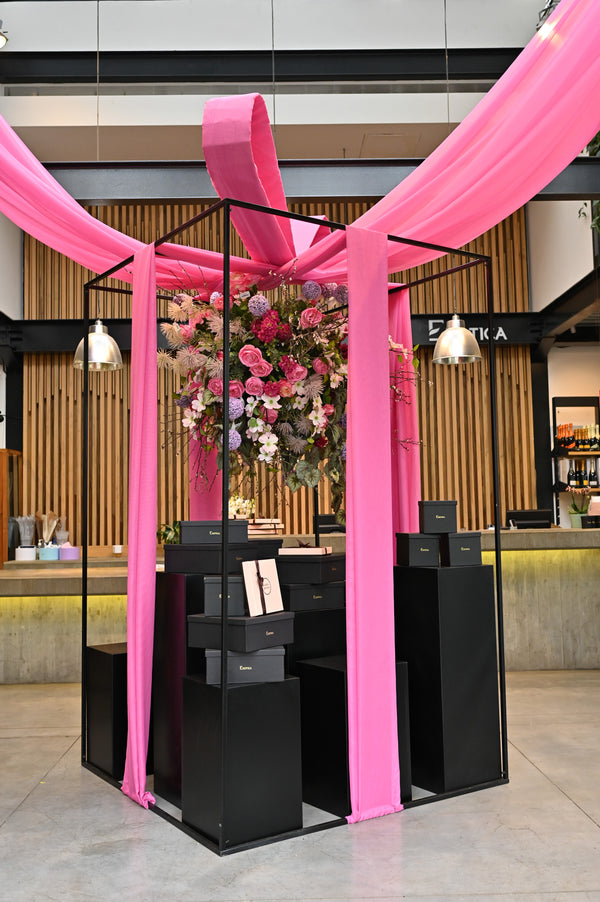 Gift display draped in pink ribbon beneath a hanging arrangement of pink roses and hydrangeas